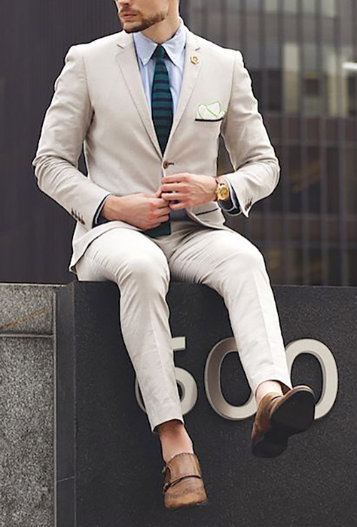 beige suit matched with a pale blue shirt, brown shoes, and dark green tie